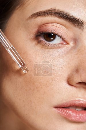 A close-up of a young Caucasian woman with clean skin applying serum with cosmetic pipette