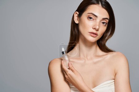 A young Caucasian woman gracefully holds a bottle with serum, exuding elegance and purity.