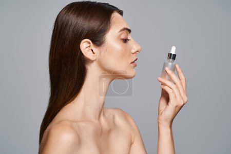 Brunette woman holding bottle with serum, nurturing her skin in a studio setting.