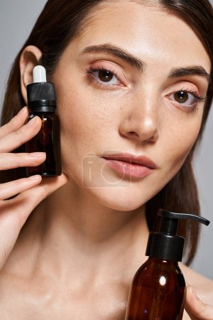 Photo for A young Caucasian woman with brunette hair holding different cosmetic bottles in studio - Royalty Free Image