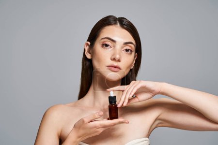 Une jeune femme caucasienne aux cheveux bruns tenant une bouteille de soin de la peau, mettant en valeur un teint radieux et sain.