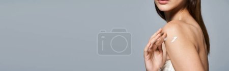 Photo for A young Caucasian woman with brunette hair strikes a pose with body cream on shoulder, exuding elegance, banner - Royalty Free Image