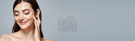 Foto de Mujer caucásica con cabello moreno toca suavemente su cara y aplica crema, tranquilidad y cuidado personal, pancarta - Imagen libre de derechos