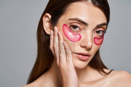 A young Caucasian woman with brunette hair wearing vibrant pink eye patches on her face, creating a bold and artistic look.