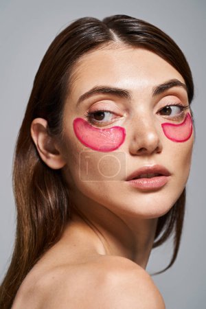 Eine junge kaukasische Frau mit rosa Augenklappen, die ihr Gesicht in einem Studio akzentuieren.