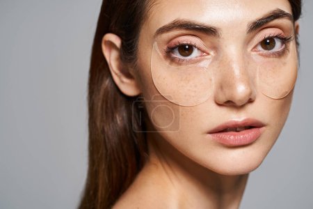Photo for A young woman with brunette hair showcases her skincare routine in under eye patches - Royalty Free Image