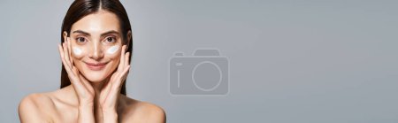 Photo for A youthful happy woman with brunette hair and flawless skin and cream on her face, banner - Royalty Free Image