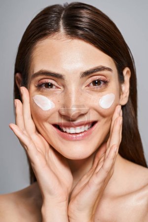 A young happy woman with brunette hair and clean skin joyfully wears a thick layer of cream on her face.