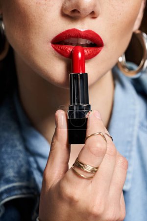 Una joven mujer sostiene un vibrante lápiz labial rojo en su mano, preparado para realzar su belleza.