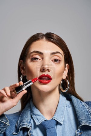 A young Caucasian woman with brunette hair gracefully applying lipstick to her lips in a studio setting.