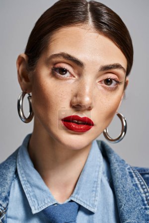 A young Caucasian woman sporting red lipstick and large hoop earrings in a studio setting.