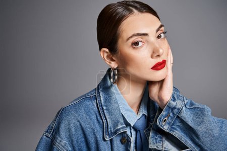 A stylish young woman with brunette hair wearing a denim jacket and red lipstick exudes confidence and elegance.