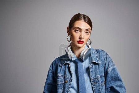 A young Caucasian woman with brunette hair wearing a denim jacket and earrings, exuding style and confidence. in headphones