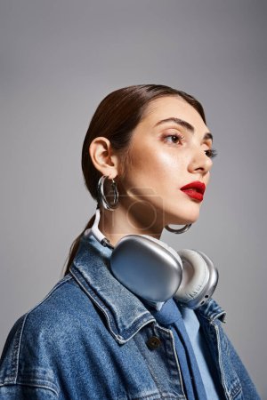 Foto de Una mujer caucásica joven con estilo en una chaqueta de mezclilla escuchando música a través de auriculares. - Imagen libre de derechos