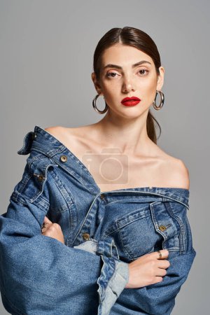 A young Caucasian woman with brunette hair wearing a trendy jean jacket and bold red lipstick.