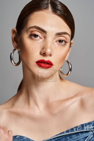 Téléchargez les photos : Une jeune femme caucasienne aux cheveux bruns, au rouge à lèvres et aux grandes boucles d'oreilles en cerceau respire la confiance et le glamour en studio. - en image libre de droit