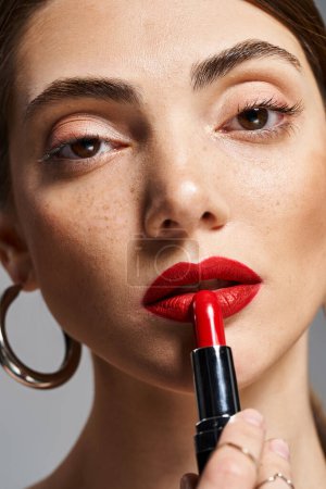 Una joven mujer caucásica con el pelo moreno usando lápiz labial rojo en los labios, exudando confianza y belleza.