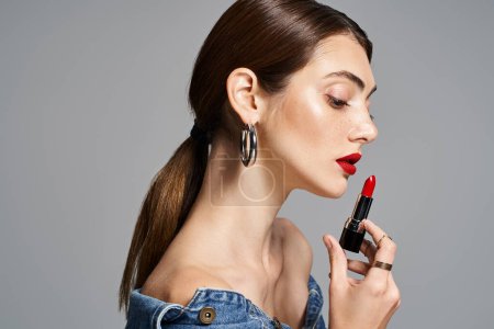 A stylish young Caucasian woman with brunette hair holds a vibrant lipstick in her hand, exuding confidence and elegance.