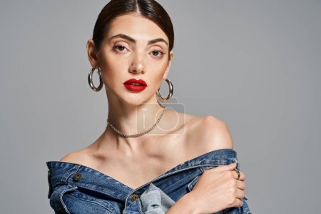 Photo for Brunette woman slaying in a denim dress, with striking red lips, exuding confidence and style in a studio setting. - Royalty Free Image