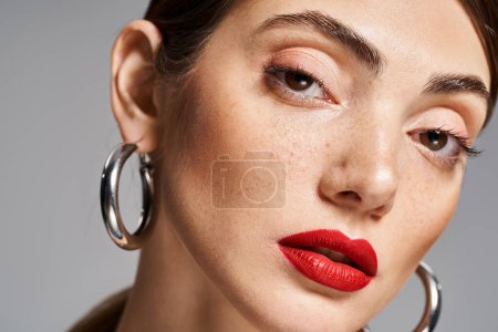 A young Caucasian woman with brunette hair sporting red lipstick and hoop earrings exudes confidence and style.