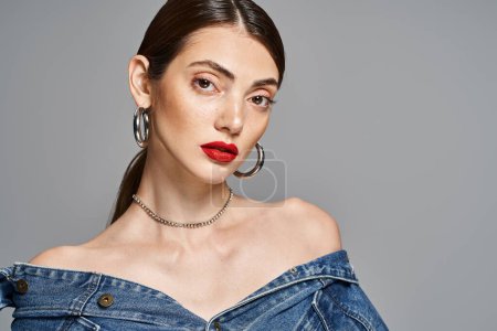 A stylish young woman with brunette hair wearing a denim dress and bright red lipstick.