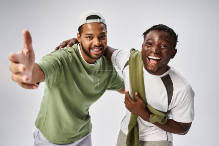 Konzept vom Juni, fröhliche afrikanisch-amerikanische Freunde gestikulieren und umarmen auf grauem Hintergrund