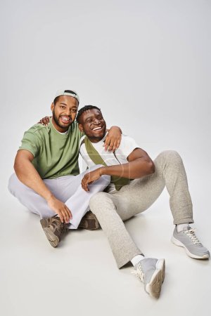 Juni-Feier, aufgeregte und junge afrikanisch-amerikanische männliche Freunde umarmen sich auf grauem Hintergrund
