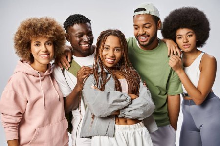 positive femme afro-américaine posant des amis proches en vêtements de sport sur fond gris, le 10 juin