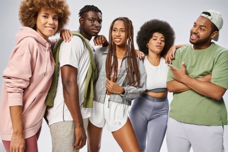 optimistische afrikanisch-amerikanische Freunde in Sportbekleidung stehen zusammen vor grauem Hintergrund, Juni