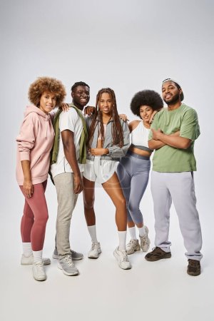 fröhliche afrikanisch-amerikanische Freunde in Sportbekleidung stehen zusammen vor grauem Hintergrund, Juni