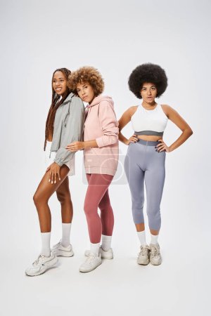 hübsche afrikanisch-amerikanische Freundinnen in Sportbekleidung schauen in die Kamera vor grauem Hintergrund, Juni