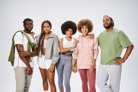Gruppe fröhlicher afrikanisch-amerikanischer Menschen in Sportbekleidung, die zusammen auf grauem Hintergrund stehen, Gemeinschaft