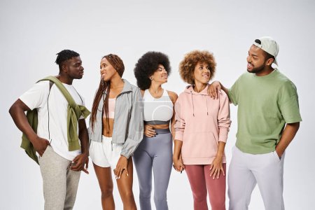 Gruppe junger afrikanisch-amerikanischer Menschen in Sportbekleidung, die zusammen auf grauem Hintergrund stehen, Gemeinschaft