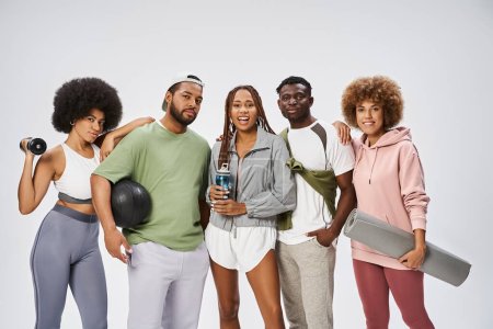 Gruppe junger afrikanisch-amerikanischer Freunde steht mit Sportgeräten vor grauem Hintergrund