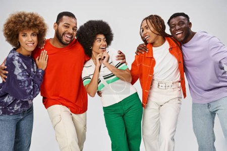 fröhliche afrikanisch-amerikanische Menschen in farbenfroher Freizeitkleidung lachen gemeinsam auf grauem Hintergrund