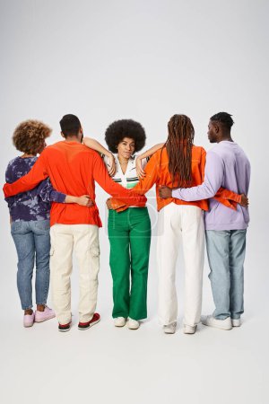 mujer afroamericana rizada apoyada en amigos abrazándose sobre fondo gris, concepto Juneteenth