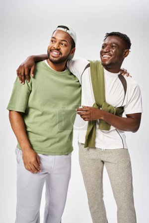 positive african american male friends in casual wear hugging on grey background, Juneteenth