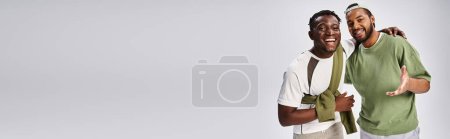 smiling african american male friends in casual wear hugging on grey background, Juneteenth banner
