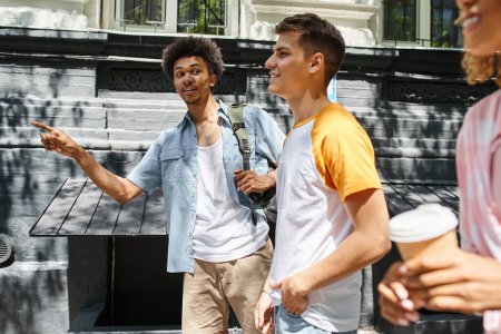 young african american man pointing with finger near cheerful multiethnic friends walking in city