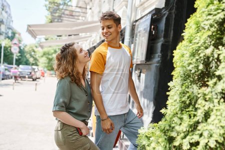 Téléchargez les photos : Jeune et élégant couple souriant à l'autre près de l'auberge de jeunesse dans la rue urbaine, les voyageurs - en image libre de droit