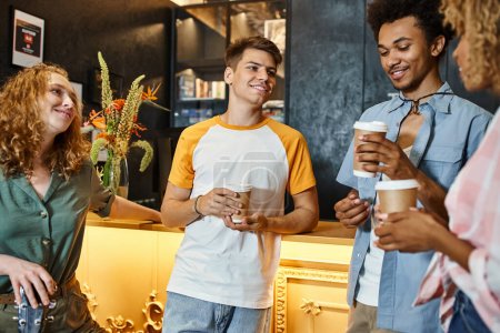 joyous multiethnic buddies with takeaway drinks talking at reception desk in youth hostel, travel