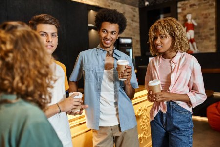 fröhliche multiethnische Freunde mit Pappbechern im Gespräch an der Rezeption in der Jugendherberge, Reisende