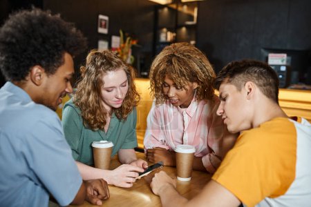 Téléchargez les photos : Jeune femme naviguant sur Internet sur smartphone près d'amis multiethniques dans le café de l'auberge de jeunesse - en image libre de droit