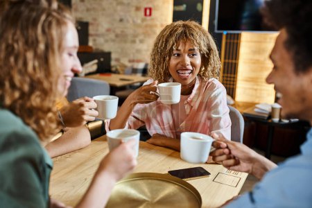 Téléchargez les photos : Heureux étudiants multiethniques boire du café et parler dans le café de l'auberge de jeunesse moderne, amitié - en image libre de droit