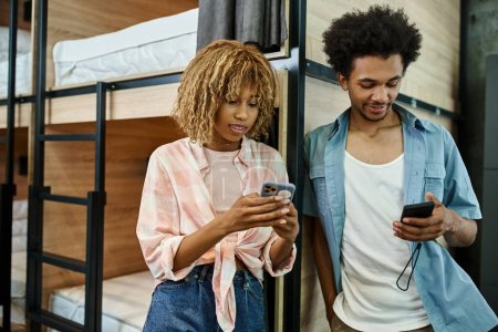 stylish african american roommates using smartphones near double-decker beds in cozy students hostel