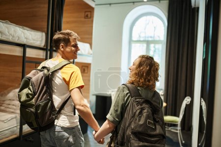 Photo for Happy young couple with backpacks holding hands and looking at each other in cozy room of hostel - Royalty Free Image