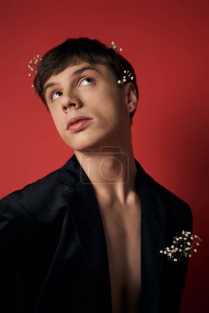 gut aussehender junger Mann im Samtblazer mit Blumen im Haar schaut in die Kamera auf rotem Hintergrund