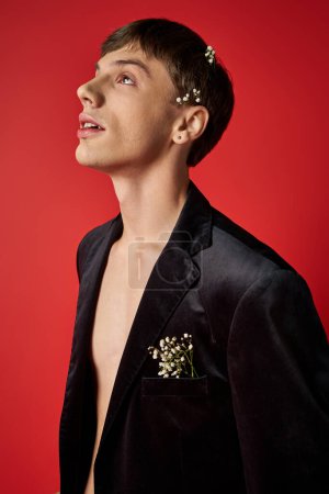 dreamy young male model in velvet blazer with flowers in hair looking up on red background