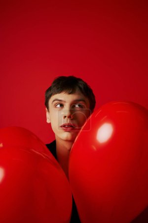 romantische und verträumte Mann in der Nähe herzförmigen Luftballons auf rotem Hintergrund, Valentinstag-Konzept