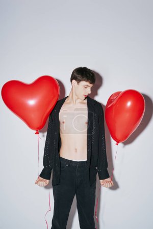 young man in black shiny open shirt holding red balloons on grey background, Valentines day